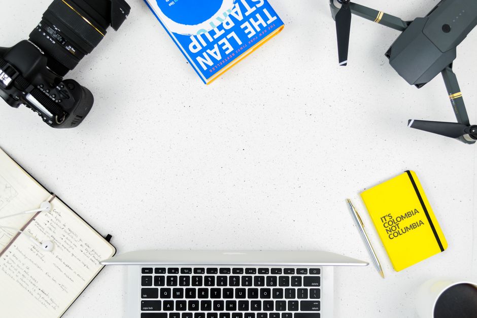 Flat lay of a creative workspace featuring a camera, drone, and laptop on a white surface.