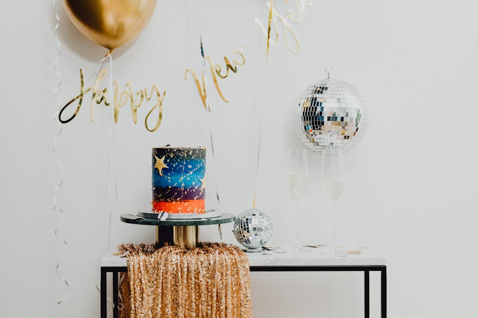 Glamorous New Year's party setup featuring a cake, balloons, confetti, and disco balls.