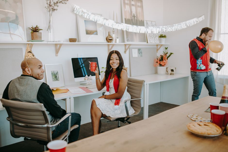 A lively office holiday celebration with three coworkers enjoying festive decorations.